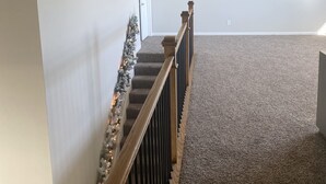 Una escalera alfombrada con barandilla de madera, paredes blancas y una lámpara en el techo.