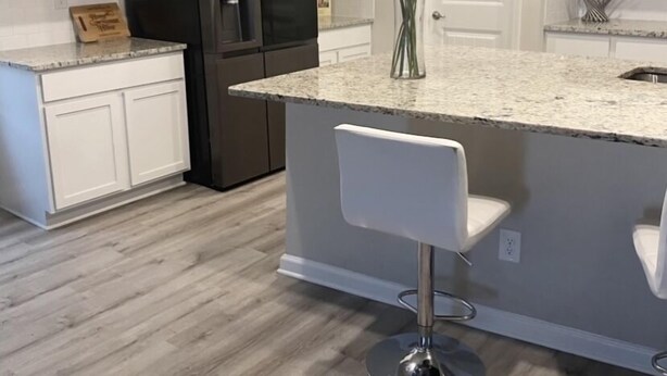 Una cocina moderna con armarios blancos, un refrigerador de acero inoxidable, una encimera de mármol y dos taburetes de bar.