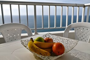 Ein Tisch mit Obstschale, gefüllt mit Bananen, einem Apfel und einer Birne, mit Blick aufs Meer.