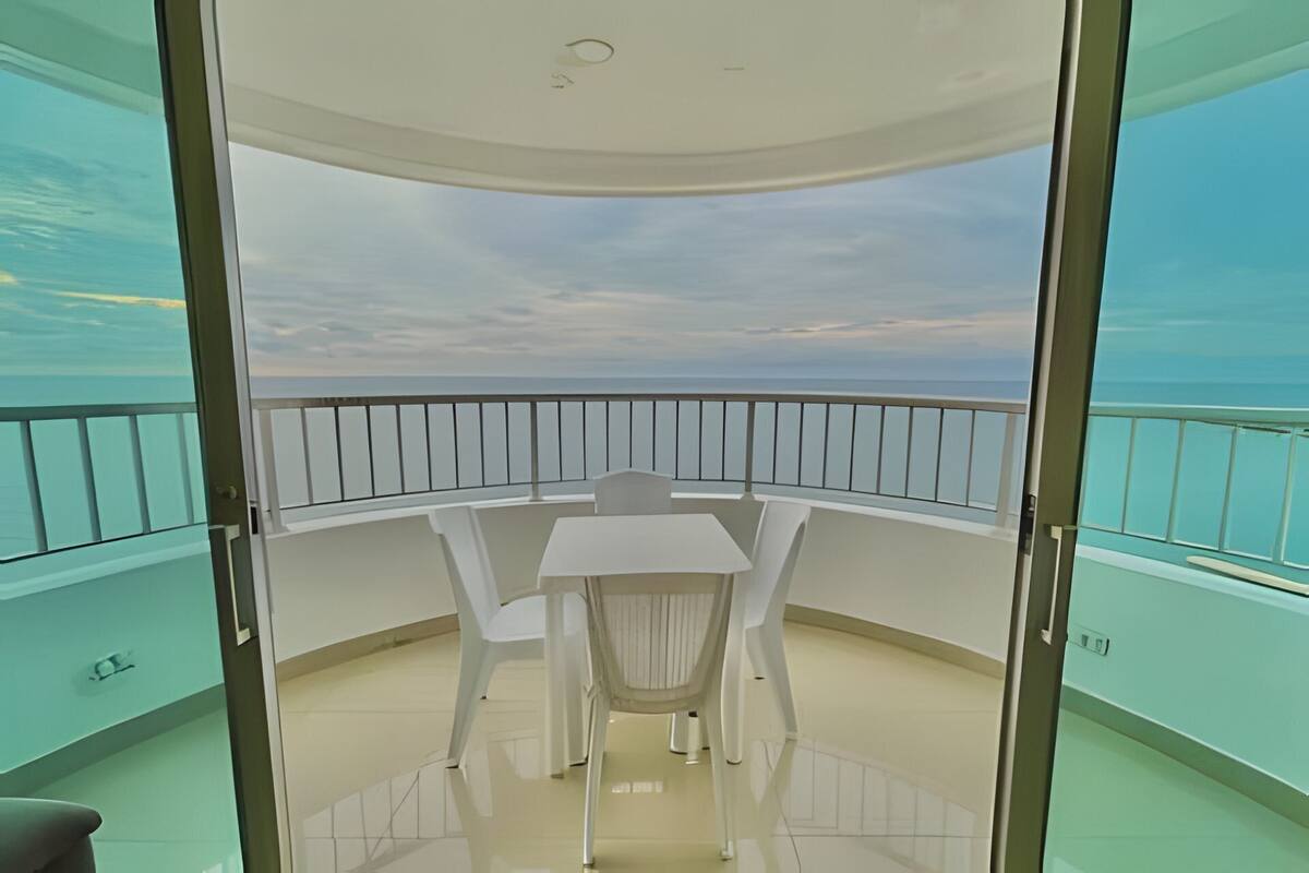 A balcony with a white table and chairs, a glass door, and a view of the ocean.