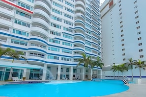 Ein modernes Hotel mit Pool, mehreren Balkonen und einem hoch aufragenden Gebäude im Hintergrund.