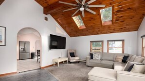 A spacious living area with a high ceiling, a ceiling fan, and a large flat-screen TV mounted on the wall.