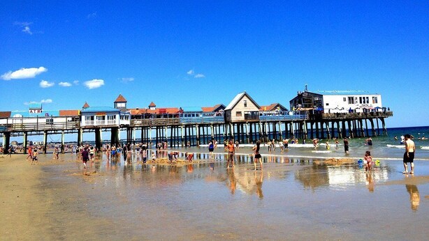 A pier with buildings and people on a beach.