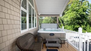 A covered porch with a hot tub, wicker furniture, and a white fence.