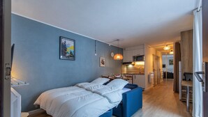 A bedroom with a bed, a desk, and a chair. There is a kitchen area with a microwave and a sink. - Le Bastan - Appt pour 4 avec Jardin (Barèges)