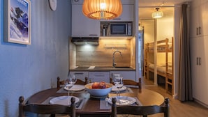 A compact kitchen with modern appliances, a dining area with a wooden table and chairs, and a cozy sleeping area with bunk beds. - Le Bastan - Appt pour 4 avec Jardin (Barèges)