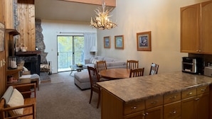 A spacious living area with a fireplace, a dining table, and a kitchen with wooden cabinets and granite countertops. - Spacious 3Bed condo 5 min from Winter Park, walk 2 Town & steps from bus stop! (Winter Park)