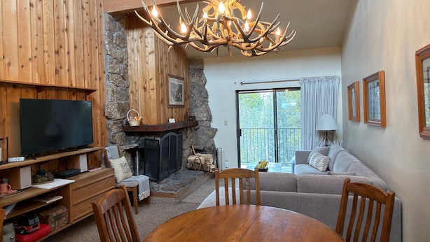 A cozy living room with a stone fireplace, a wooden TV stand, a dining table, and a sofa. - Spacious 3Bed condo 5 min from Winter Park, walk 2 Town & steps from bus stop! (Winter Park)