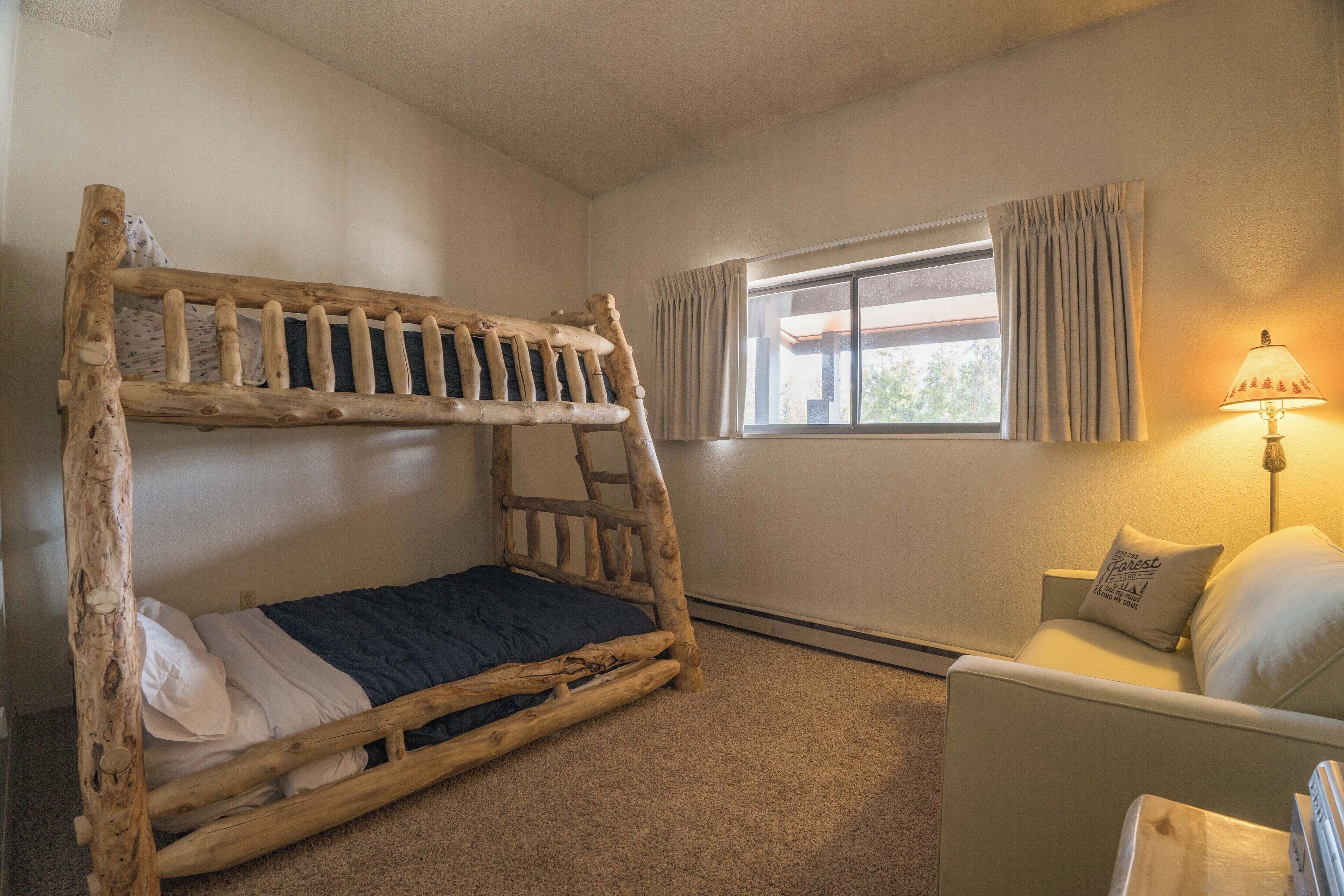 Una habitación con una cama litera, un sofá, una lámpara y una ventana con cortinas.