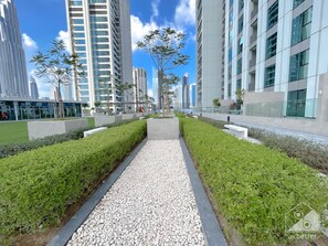 Stroll along the well-maintained pathway surrounded by lush greenery and contemporary high-rise buildings.