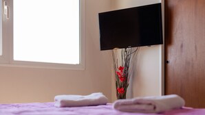 A neatly made bed with a purple bedspread and two folded white towels. A flat-screen TV is mounted on the wall above the bed. - Apartments Bariloche - Downtown, Mitre (San Carlos de Bariloche)