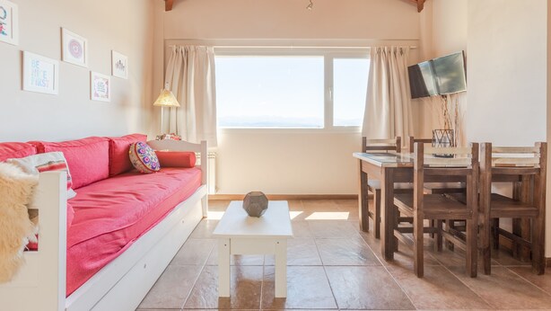 A cozy living room with a red sofa, a white coffee table, and a dining area with wooden chairs and a table. - Apartments Bariloche - Downtown, Mitre (San Carlos de Bariloche)