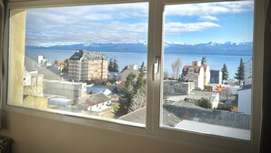 A view from a window overlooking a lake with buildings and mountains in the background. - Apartments Bariloche - Downtown, Mitre (San Carlos de Bariloche)