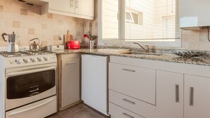 A modern kitchen with a gas stove, oven, dishwasher, and a window with blinds. - Apartments Bariloche - Downtown, Mitre (San Carlos de Bariloche)