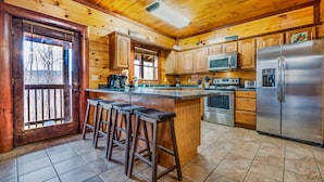 Cocina de cabaña de madera con una isla central, taburetes de bar, refrigerador, microondas, horno y armarios de madera.