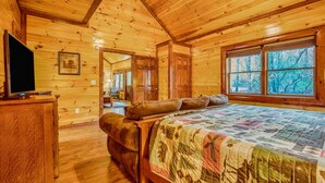 Un dormitorio acogedor tipo cabaña de madera con una cama grande, paredes de madera y una ventana con vistas a árboles.