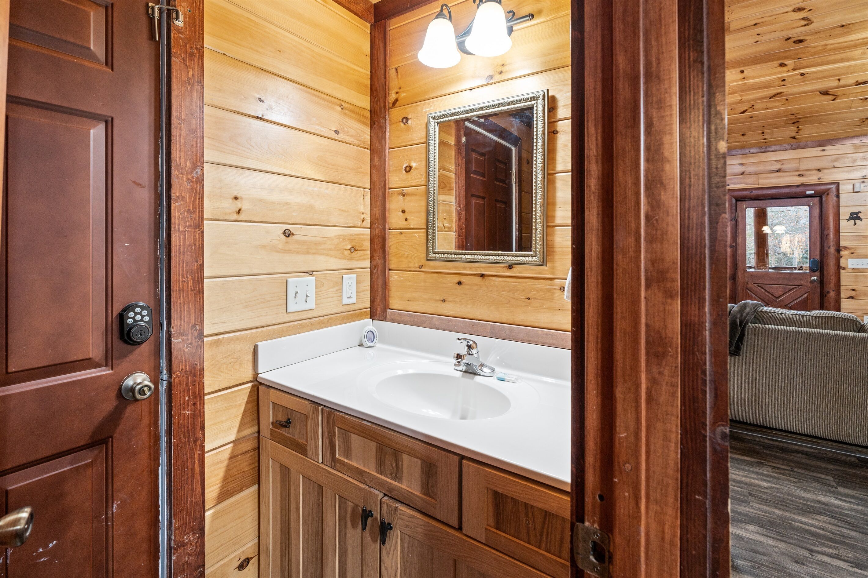 A wooden cabin bathroom with a white sink, wooden cabinets, a mirror, and a door with a handle.