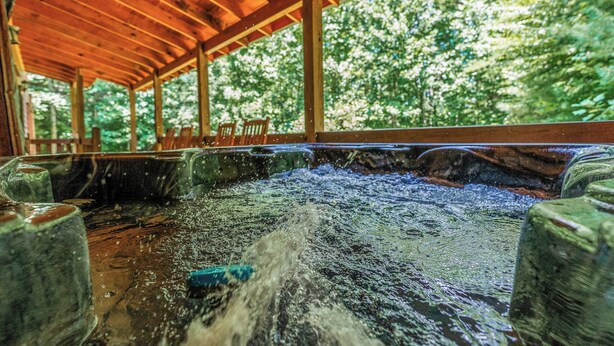A wooden covered hot spring area with benches and a view of trees. - Heated Pool, Theater, Game Room | Sleeps 25 (Cosby)