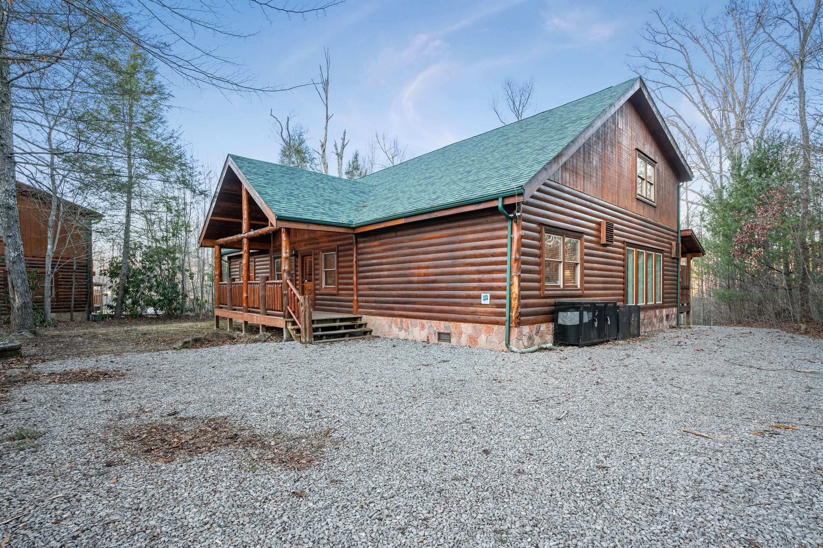 A log cabin with a green roof, wooden porch, and a gravel driveway.