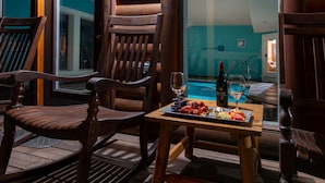 A wooden deck with two chairs, a table with a bottle of wine, a glass, and a plate of fruit. - Heated Pool, Theater, Game Room | Sleeps 25 (Cosby)