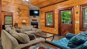 A cozy log cabin interior with a fireplace, a television, and a sofa set. - Heated Pool, Theater, Game Room | Sleeps 25 (Cosby)