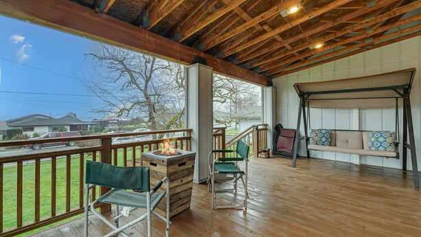 Une terrasse couverte avec un plancher en bois, un foyer, deux chaises pliantes, une balançoire et une vue sur les environs.