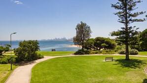 A park with a bench, a pathway, and a view of the ocean and a city skyline.
