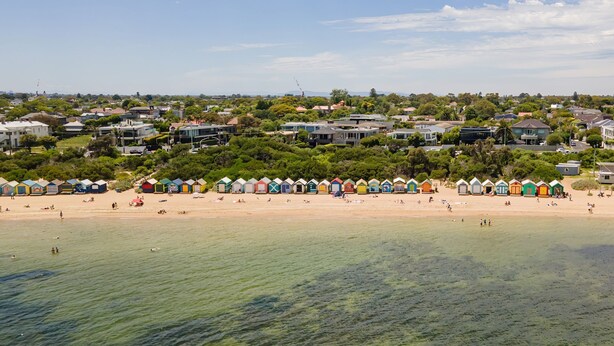 A beach with colorful beach huts and houses in the background.