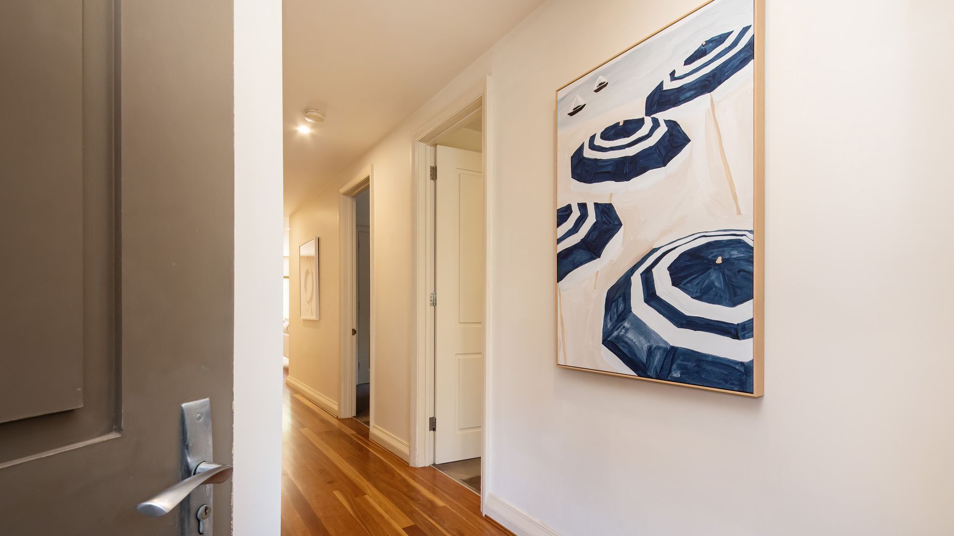 A hallway with wooden flooring, white walls, and a large abstract painting.