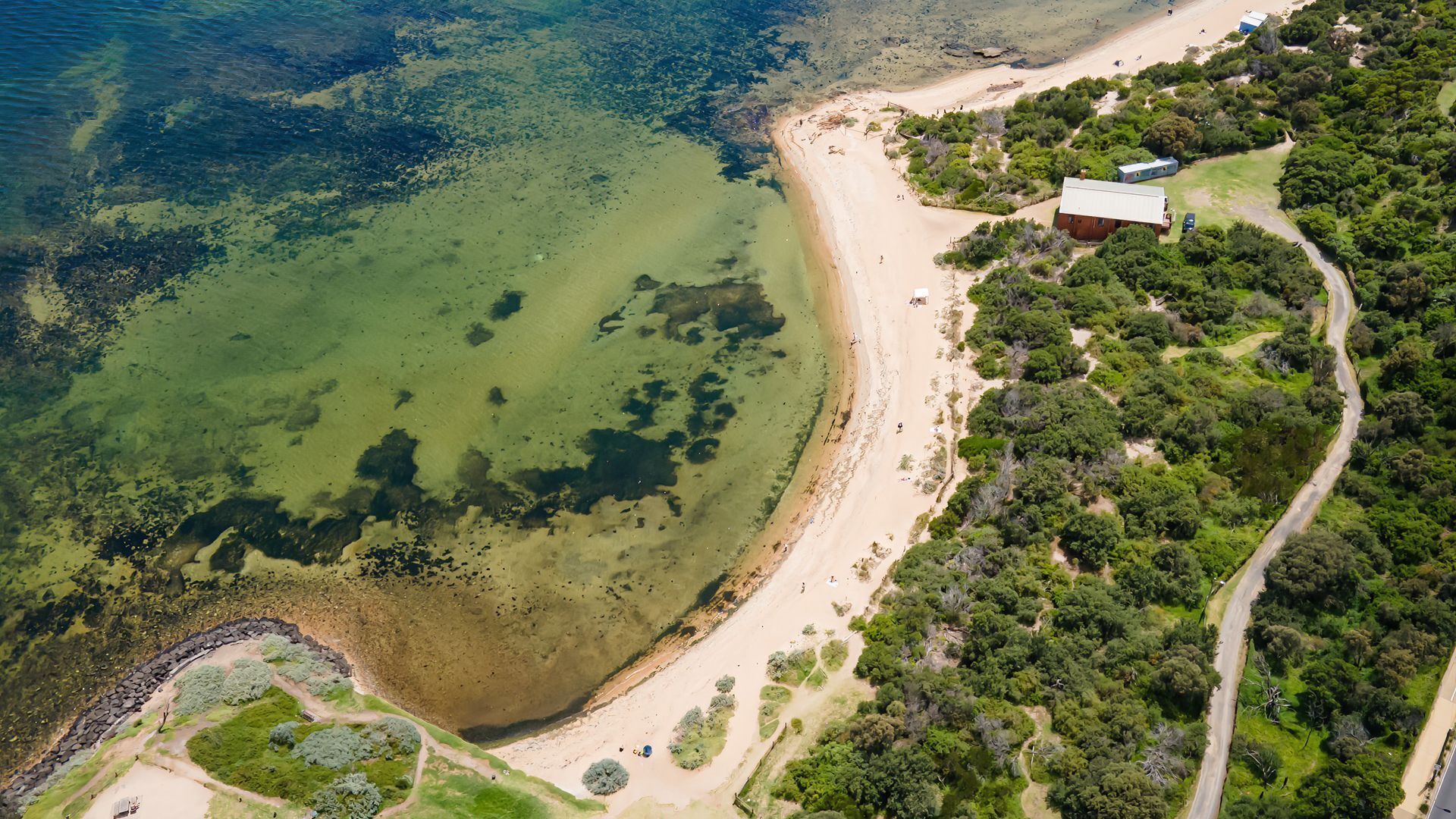 An aerial view of a coastal area with a beach, a road, and a building.
