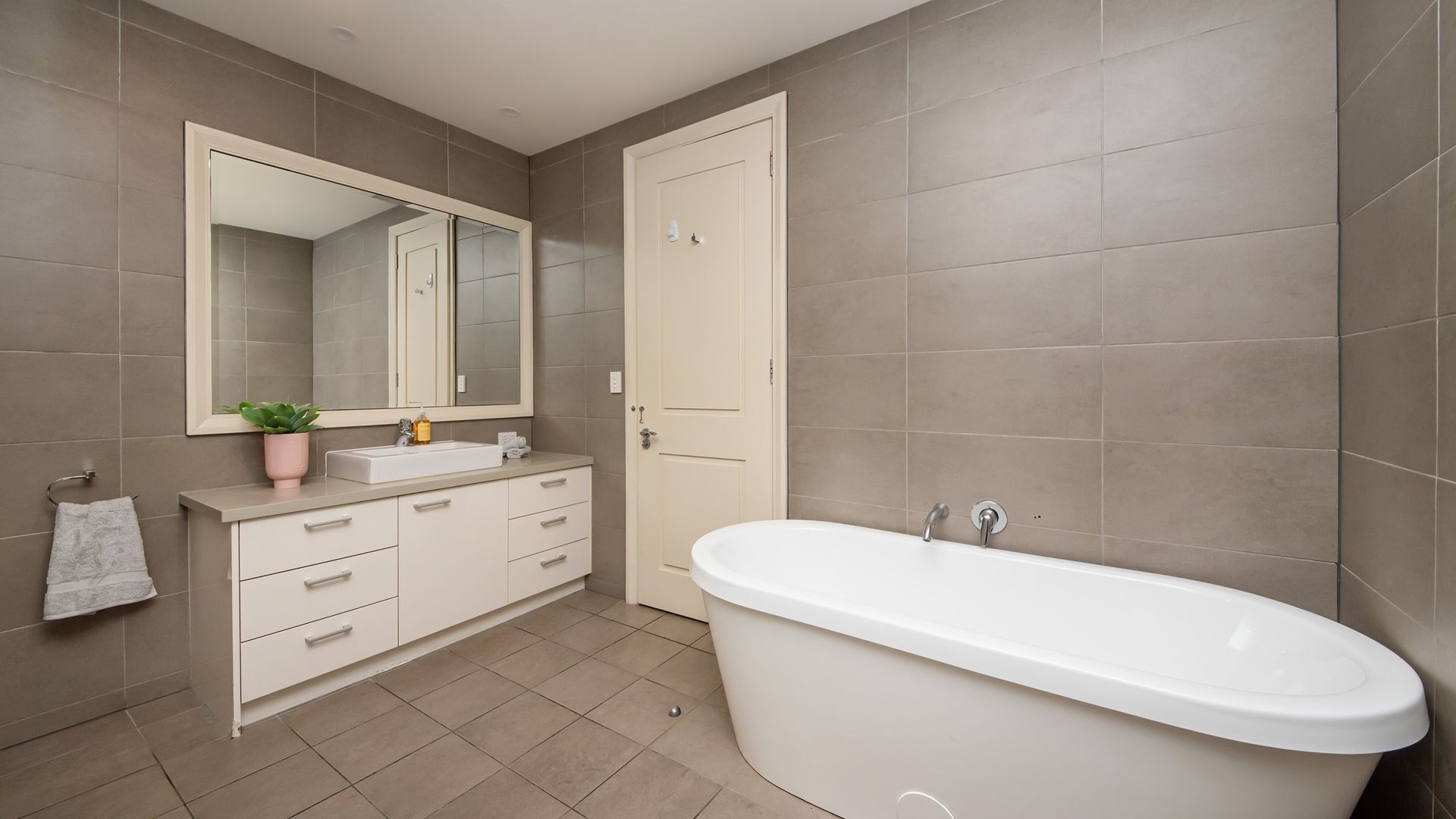 Un baño moderno con una bañera independiente, un espejo grande, un lavamanos y una puerta.
