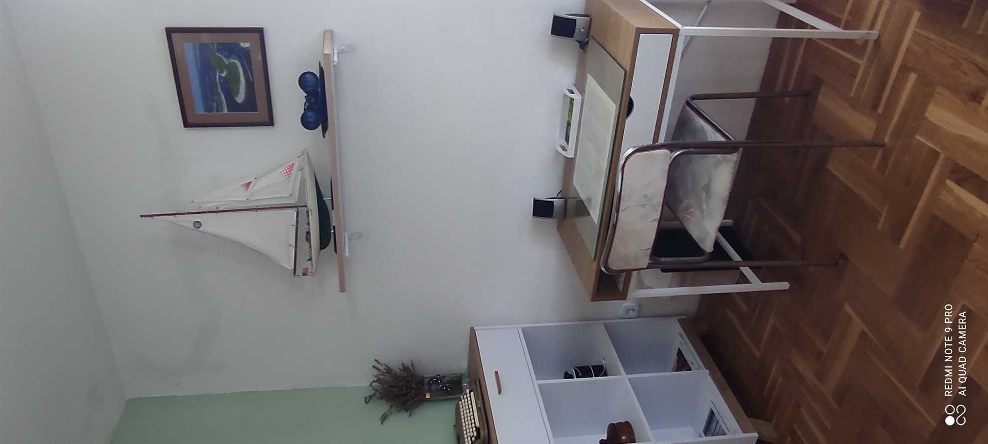 A room with a bed, a desk, a chair, a potted plant, and a framed picture on the wall.
