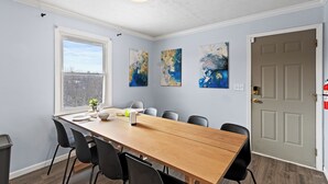 A dining area with a wooden table, black chairs, a window, and abstract wall art.