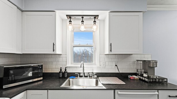 A modern kitchen with white cabinets, a stainless steel sink, a microwave, and a coffee maker.