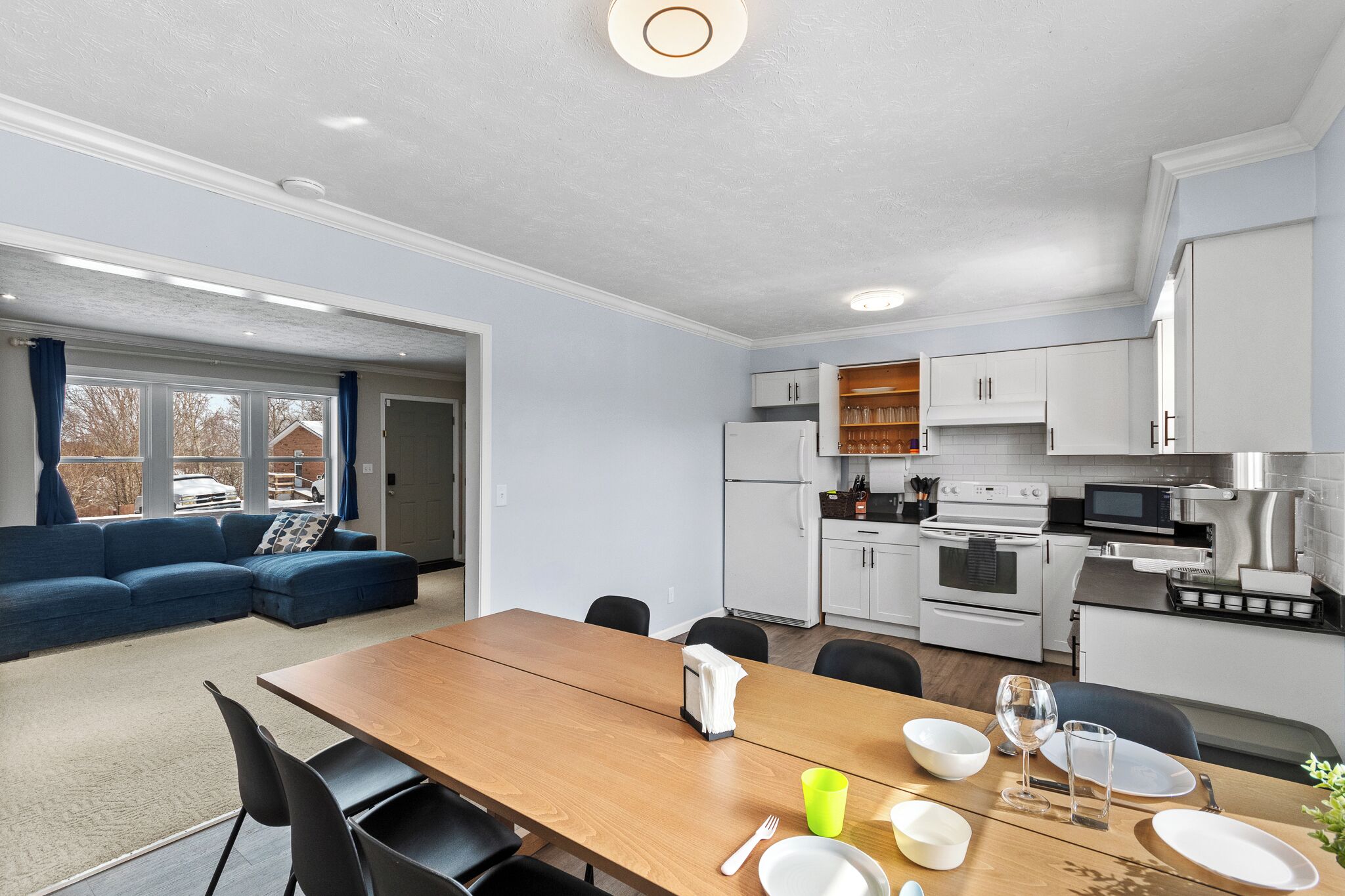 Una cocina moderna con armarios blancos, una mesa de comedor de madera y un sofá azul en la sala.