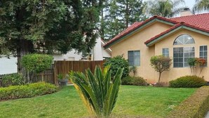 Una casa residencial amb un jardí ben cuidat, una palmera petita i un senyal de sistema de seguretat.