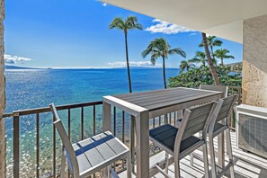 A balcony with a table and chairs overlooking a clear blue sea and palm trees. - New Luxury Oceanfront Condo ★ Amazing 180° Ocean Views ★ Top-Floor Corner-Unit (Wailuku)