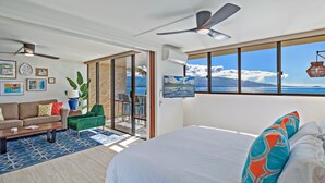 Une pièce spacieuse avec un grand lit, un canapé et une table basse. Elle dispose d’un balcon avec vue sur l’océan.