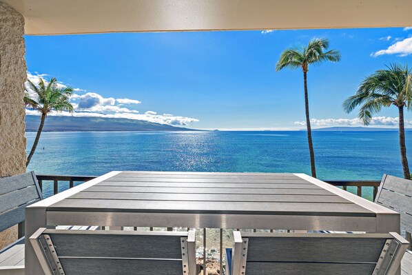A wooden table and chairs with a view of the ocean and palm trees. - New Luxury Oceanfront Condo ★ Amazing 180° Ocean Views ★ Top-Floor Corner-Unit (Wailuku)