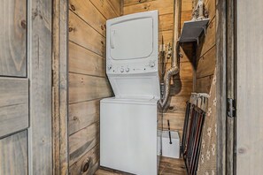 Une petite buanderie aux murs en bois, équipée d’un lave-linge et d’un sèche-linge blancs, d’un tuyau et d’un radiateur.