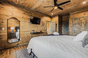 A wooden-paneled bedroom with a bed, a TV, a mirror, and a ceiling fan. - Luxury 3-story cabin! MTN Views Hot Tub, Game Room, Fire Pit, Book Fall Now! (Gatlinburg)