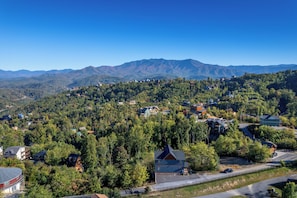 A residential area with houses surrounded by dense forest and mountains in the background. - Luxury 3-story cabin! MTN Views Hot Tub, Game Room, Fire Pit, Book Fall Now! (Gatlinburg)
