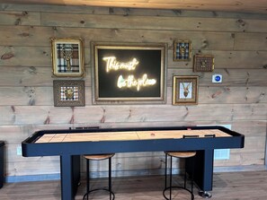 Ein Billardtisch mit einem Neonlichtschild, das "This is the place" zeigt, in einem Raum mit Holzwänden und gerahmten Bildern.