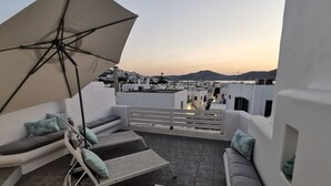 Terraza en la azotea con un sofá blanco, una silla de lounge y una sombrilla.