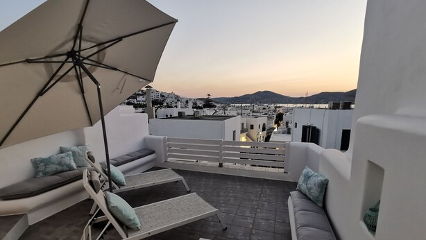 Una terrazza sul tetto con un divano bianco, una poltrona da relax e un ombrellone.