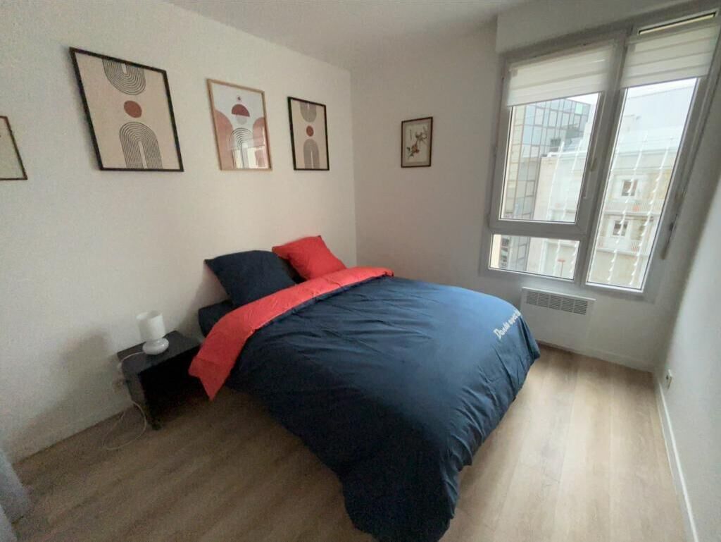 A bedroom with a bed, a nightstand, a window, and wall art.