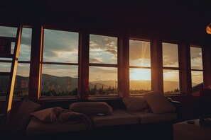 A room with a large window overlooking a landscape, a sofa, and a television.
