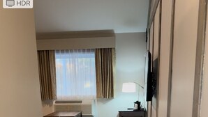 Un pasillo con piso de madera, una pequeña mesa con lámpara y una ventana con cortinas.