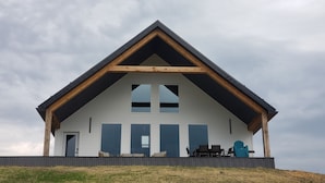 A modern house with a gabled roof, large windows, and a covered porch with outdoor furniture.