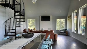 A modern kitchen with a glass dining table, a spiral staircase, and large windows.
